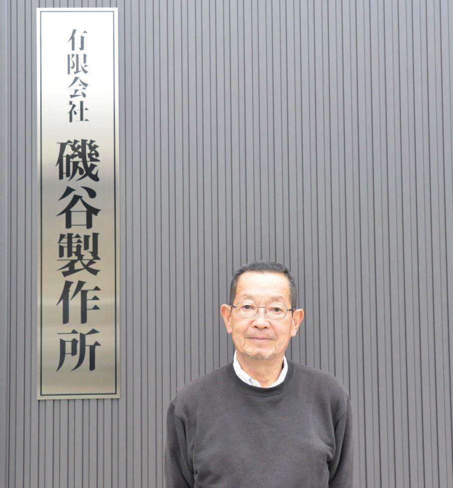 磯谷製作所の看板の前に立つ代表 磯谷金司